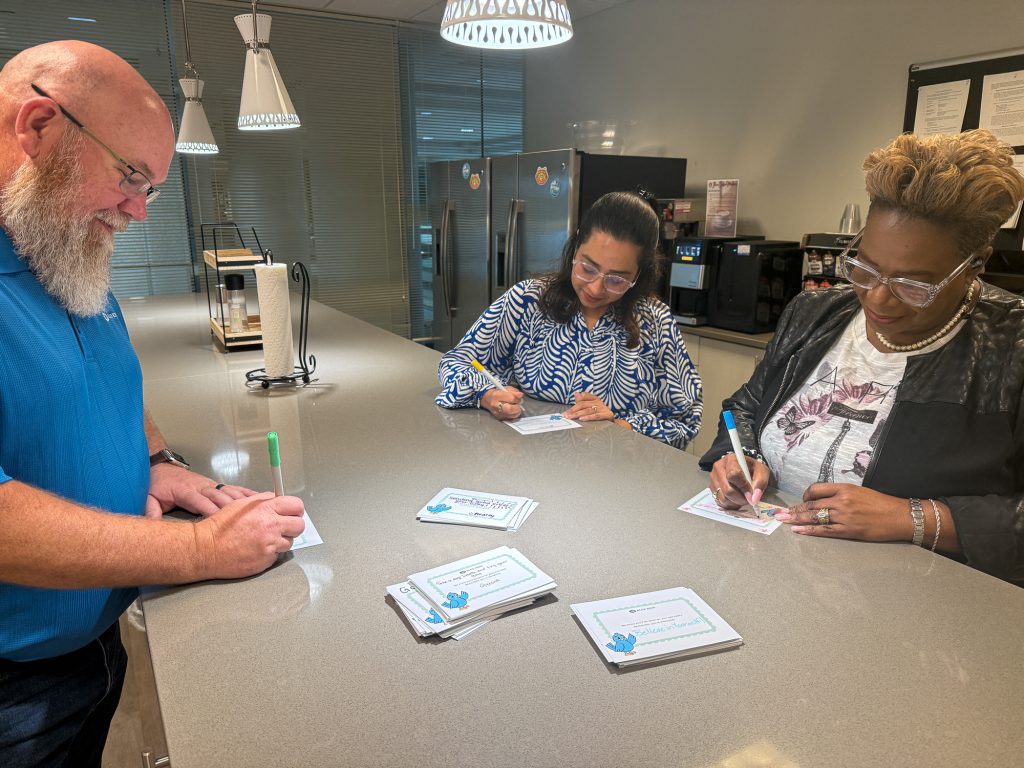Three employees stand around a counter signing cards.